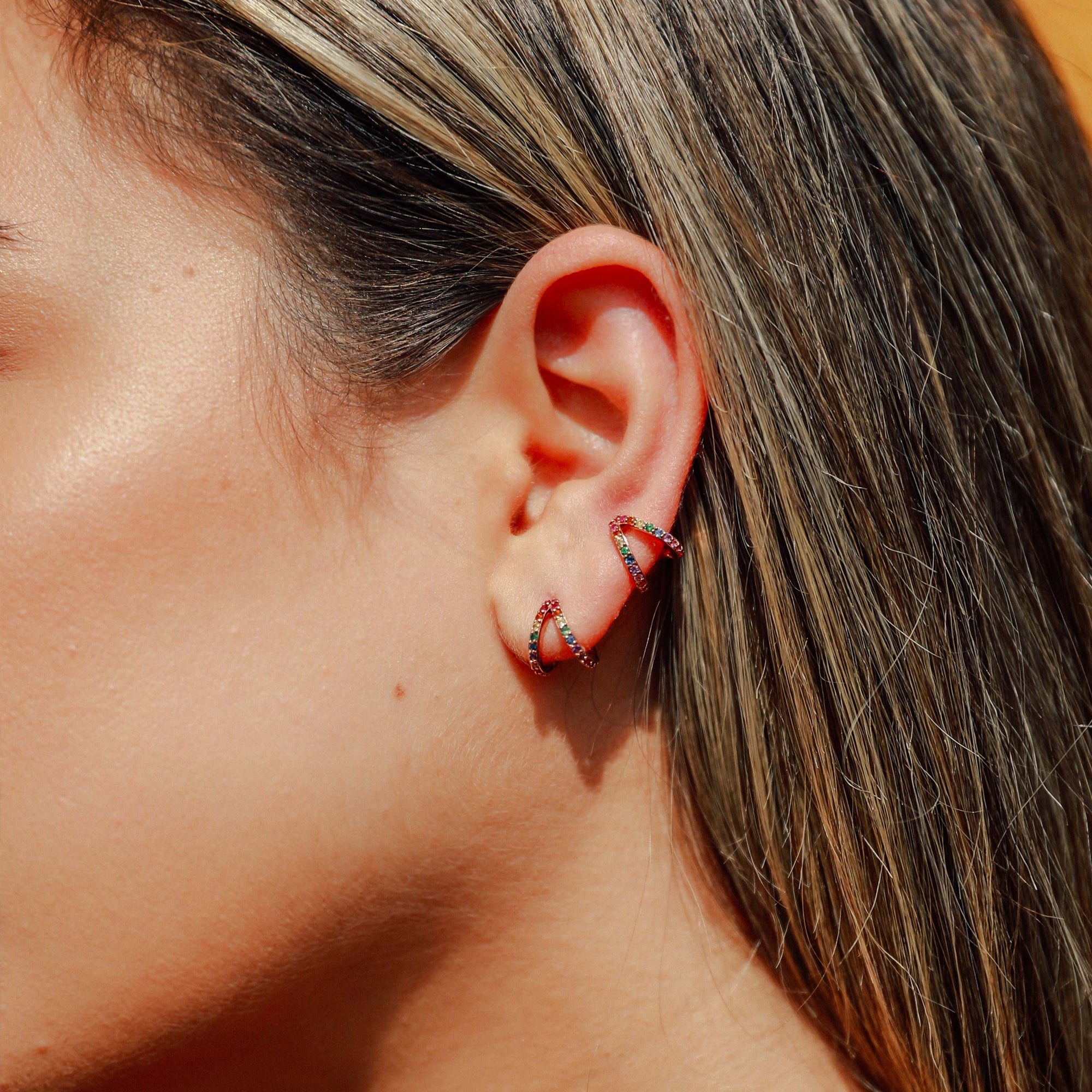 A pair of Rainbow Split Huggies shown stacked on the ear in rose gold.